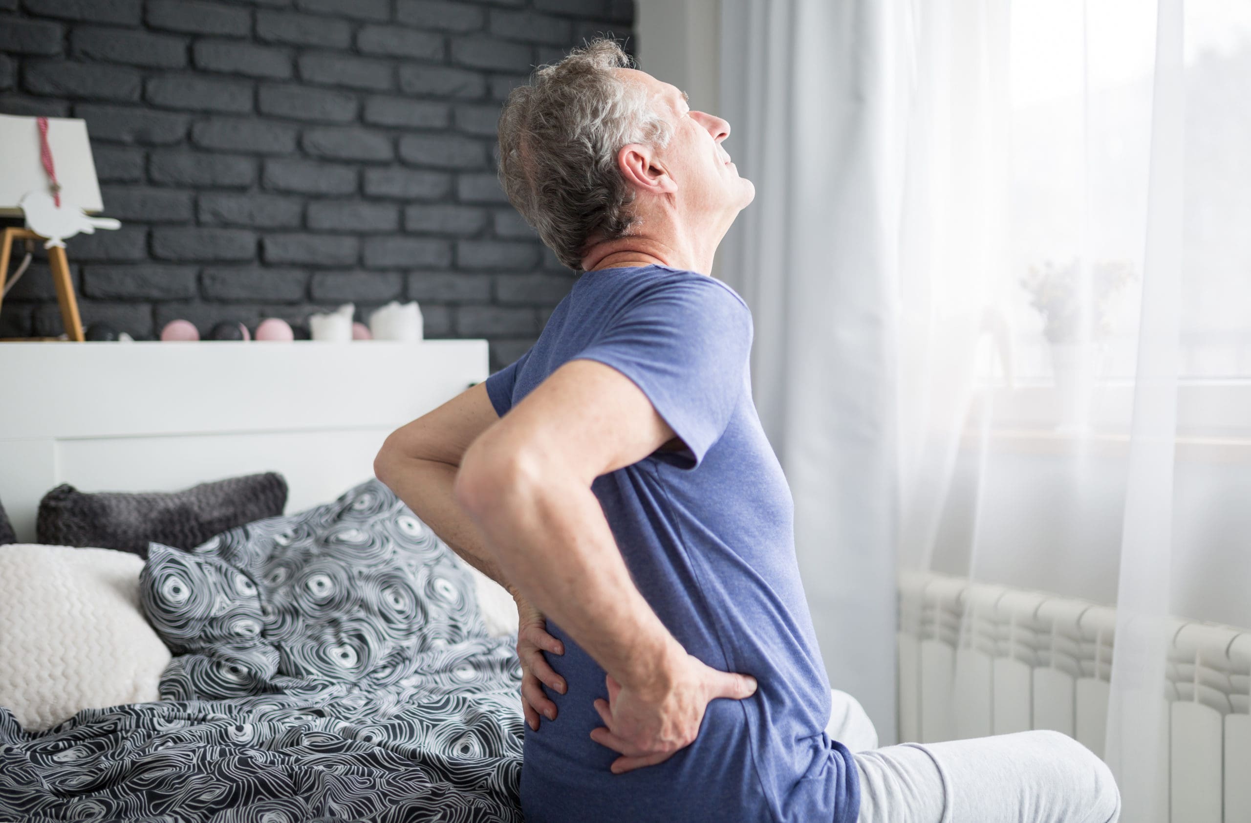 Senior man with lower back pain siting on bed