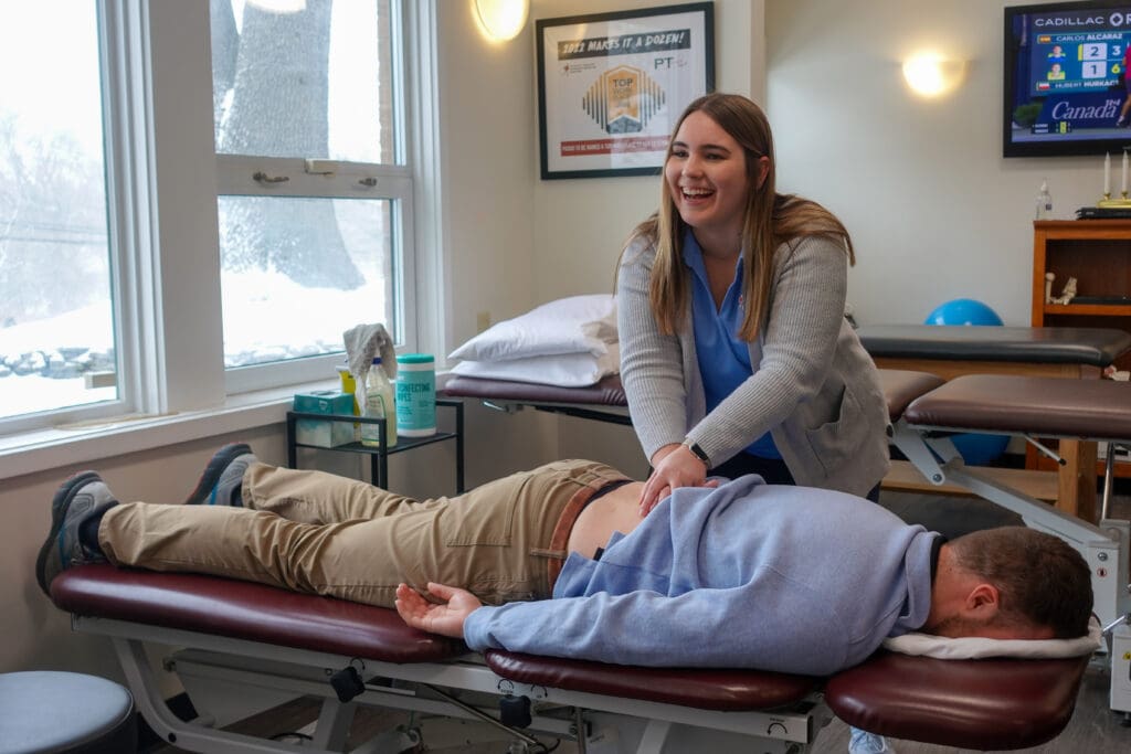 Physical Therapy & Sports Medicine Centers (PTSMC) Waterbury. Emily Pelz, female physical therapist, smiling while treating male patient's low back on treatment table